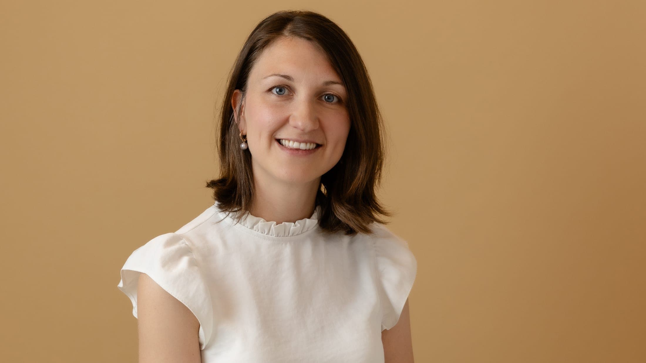 Marni Lindsay seated on a stool in a white blouse, smiling towards the camera
