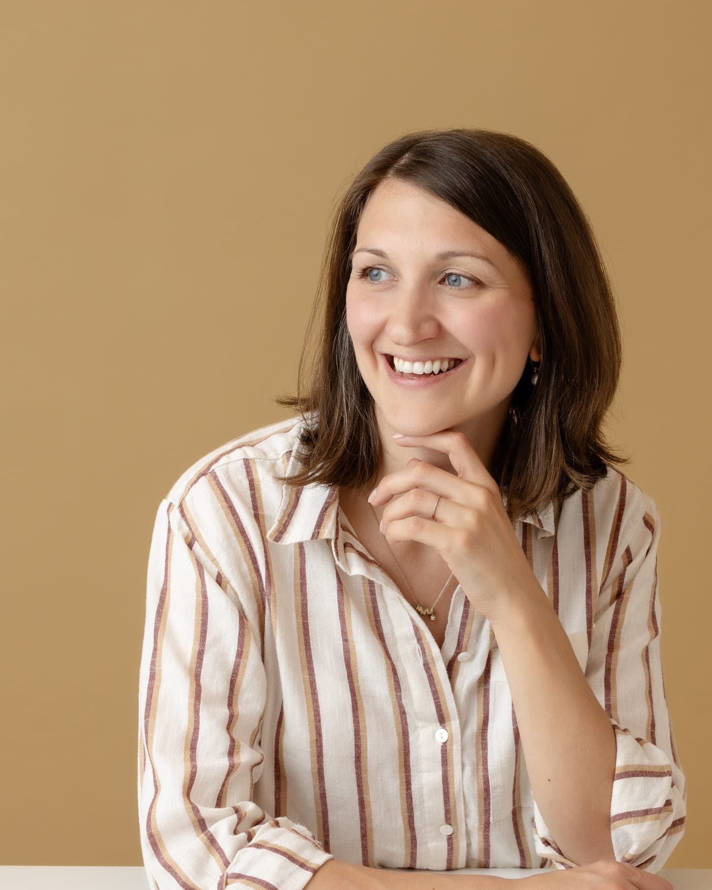 Marni Lindsay in a striped shirt, resting her chin on her hand and smiling off camera